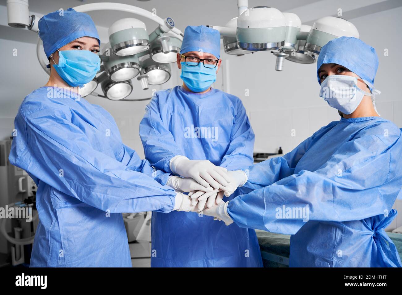 Medizinische Arbeiter verbinden ihre Hände als Symbol der Einheit. Gruppe von Ärzten mit Stapel von Händen tragen weiße sterile Handschuhe, blaue OP-Uniform. Konzept von Einheit, Teamwork und Medizin. Stockfoto