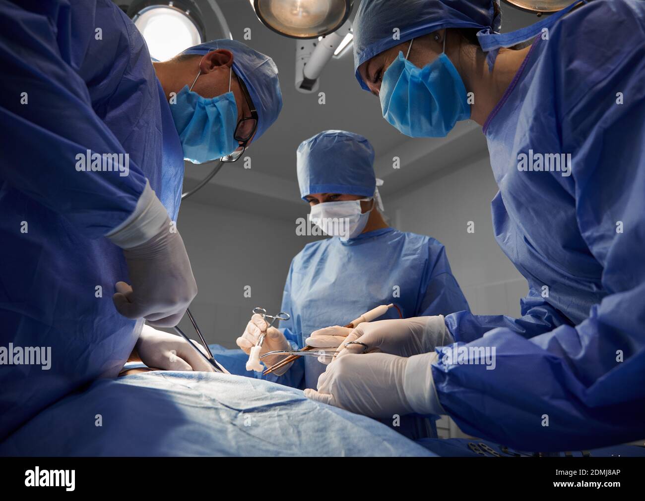 Operationsteam in blauen Anzügen mit medizinischen Instrumenten und Durchführung ästhetischer Chirurgie in der modernen Klinik. Konzept der Medizin, Bauchstraffung und plastische Chirurgie. Stockfoto