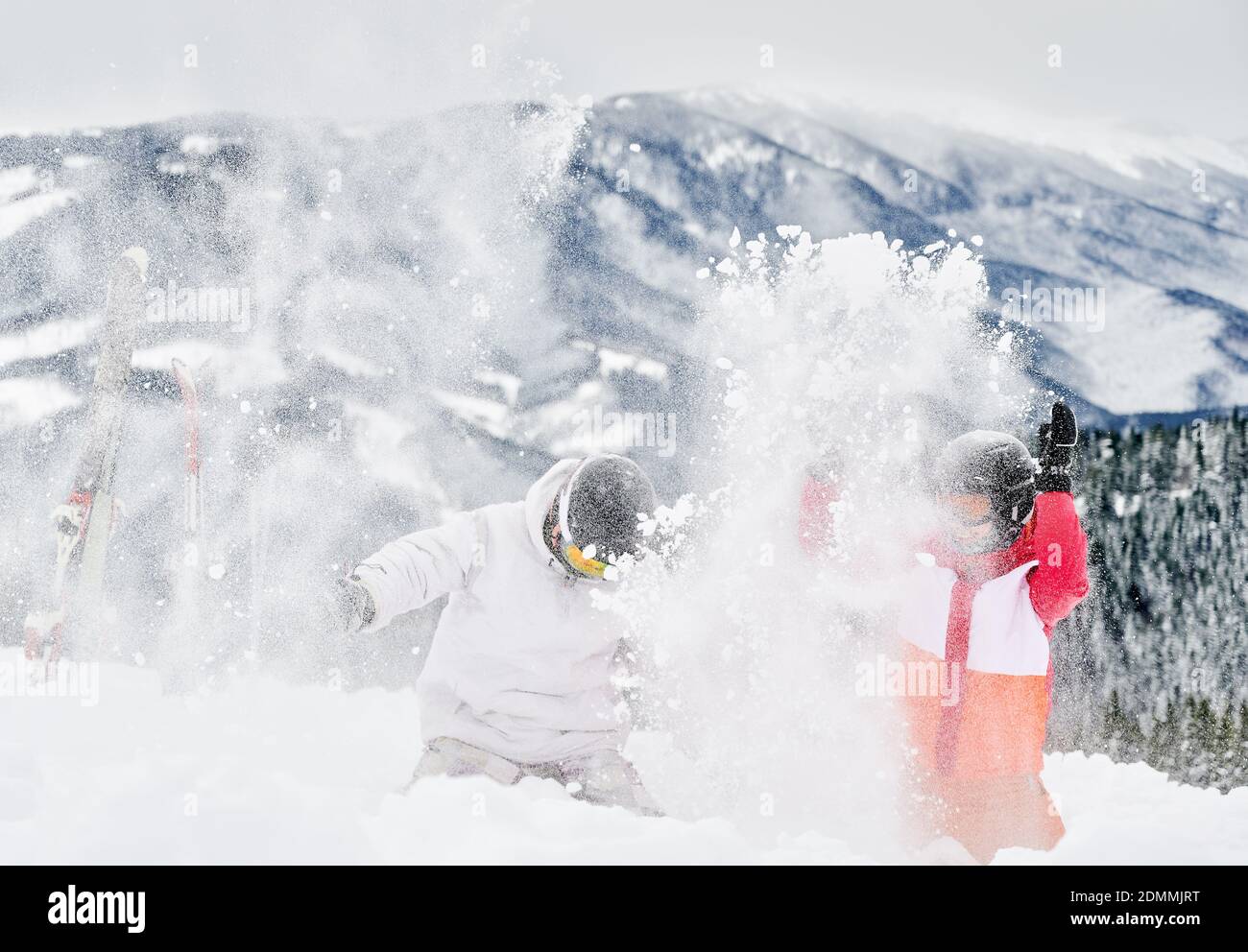 Junge Touristen spielen im Schnee gegen faszinierende Landschaften im Hintergrund und werfen Schnee. Lebendige bunte Anzüge auf weißem Schnee. Konzept für unvergessliche Momente Stockfoto