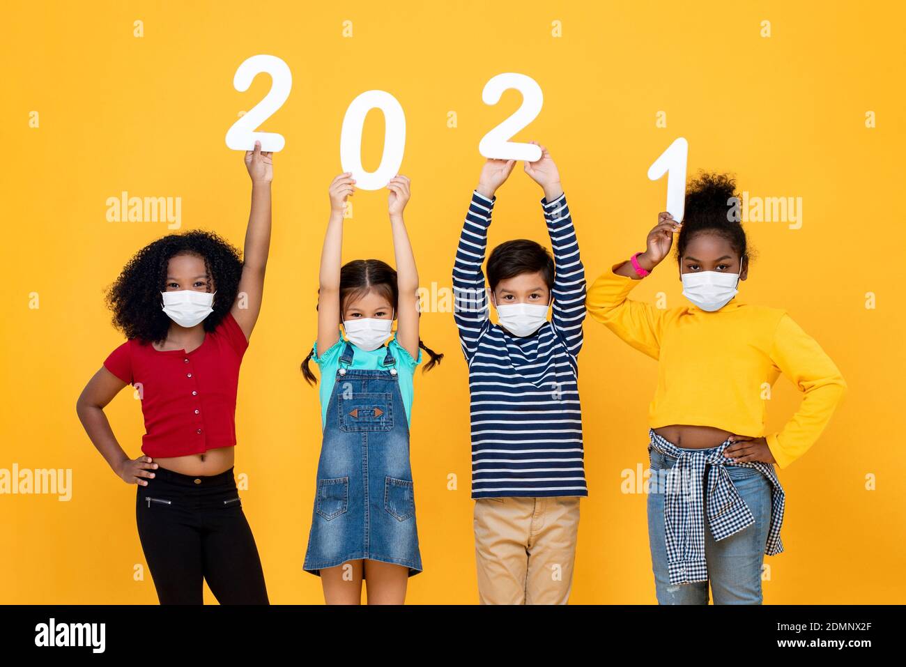 Nette gemischte Rasse Kinder tragen medizinische Gesichtsmasken halten 2021 Zahlen isoliert auf gelbem Hintergrund, Neujahr in der Zeit der Pandemie Konzepte Stockfoto