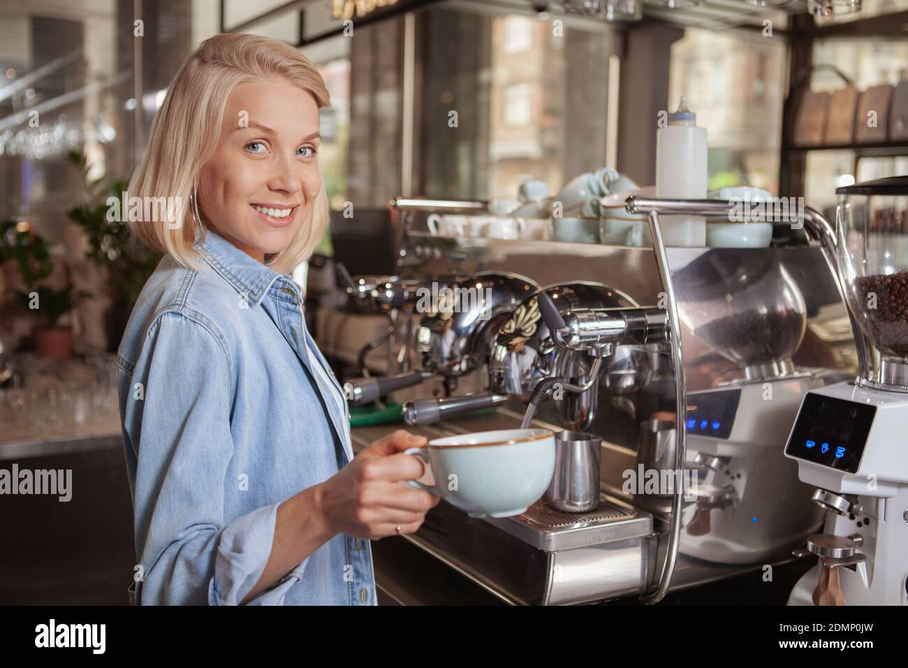 Schöne glückliche weibliche Barista hält eine Tasse köstlichen aromatischen Kaffee, lächelt auf die Kamera, kopieren Raum. Charmante Frau arbeitet bei ihrem Kaffee sho Stockfoto