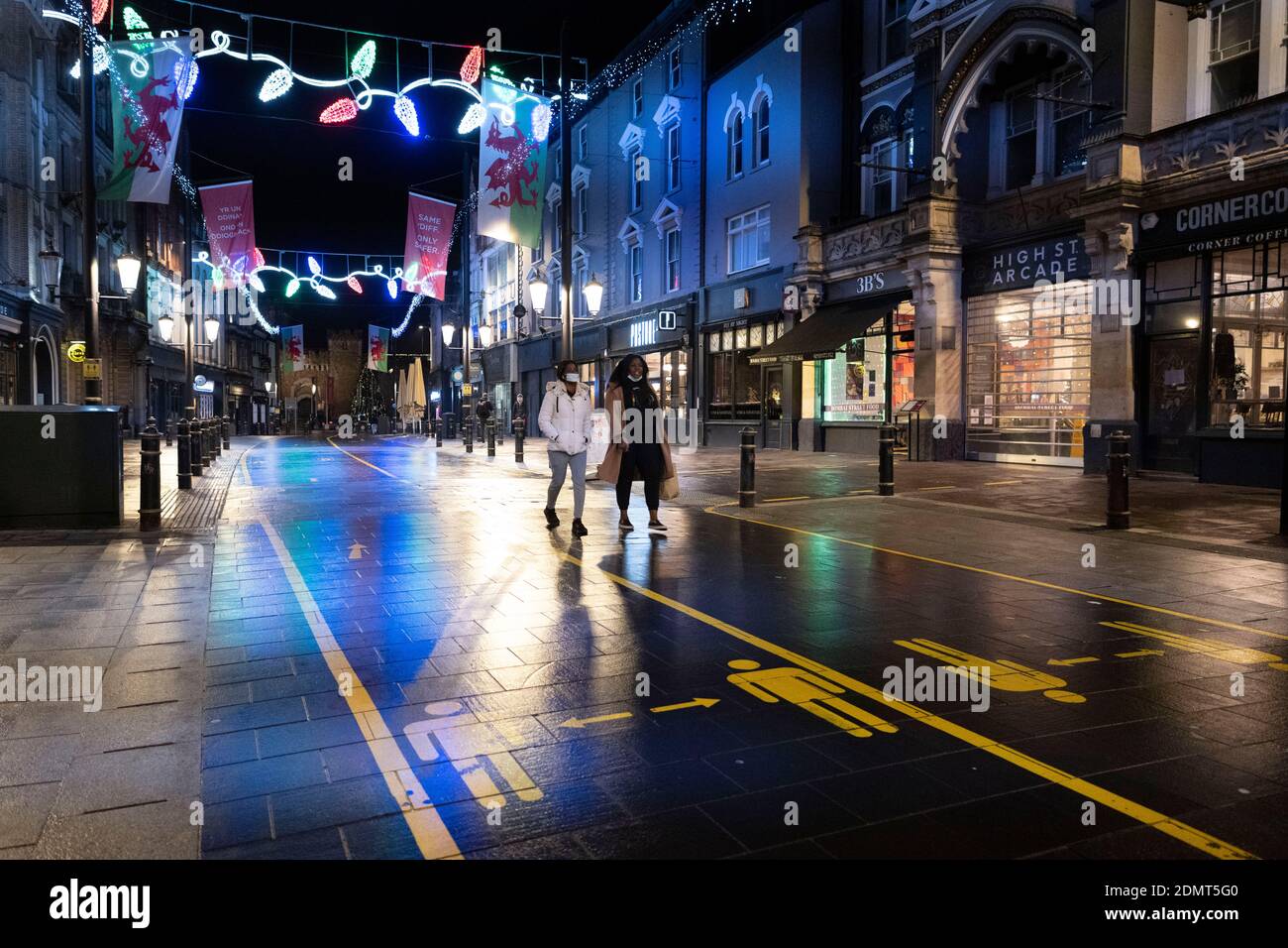 Zwei Frauen gehen in Cardiff während der Weihnachtszeit eine ruhige High Street mit sozialen Distanzschildern entlang. Stockfoto