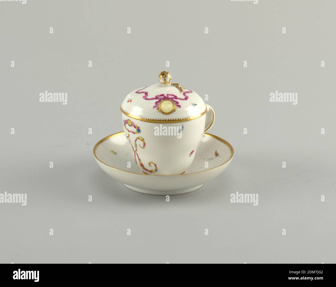 Gedeckter Becher und Untertasse, Meissener Porzellanmanufaktur, deutsch, aktiv von 1710 bis heute, Hartporzellan, Glaskerz, Gold, invertierter birnenförmiger Becher auf kleinem vergoldeten Fußrand; verschlenkter Bügelgriff, der in vergoldeten Blättern endet. Auf der gegenüberliegenden Hand ist ein großer Schriftbuchstabe gemalt, K: Von einem Kranz überragt; beide in vergoldeter Umrandung mit rosa Bändern und bunten Blumen; 3 winzige verstreute Blüten. Runder Deckel mit vergoldeten aber mit Stiel. Rosa Band umschließt Knopf, mit Schleife um vergoldeten Rahmen um den Buchstaben K gebunden, ähnlich wie die Tasse. 3 Streublumen., Deutschland, ca. 1785, Keramik Stockfoto