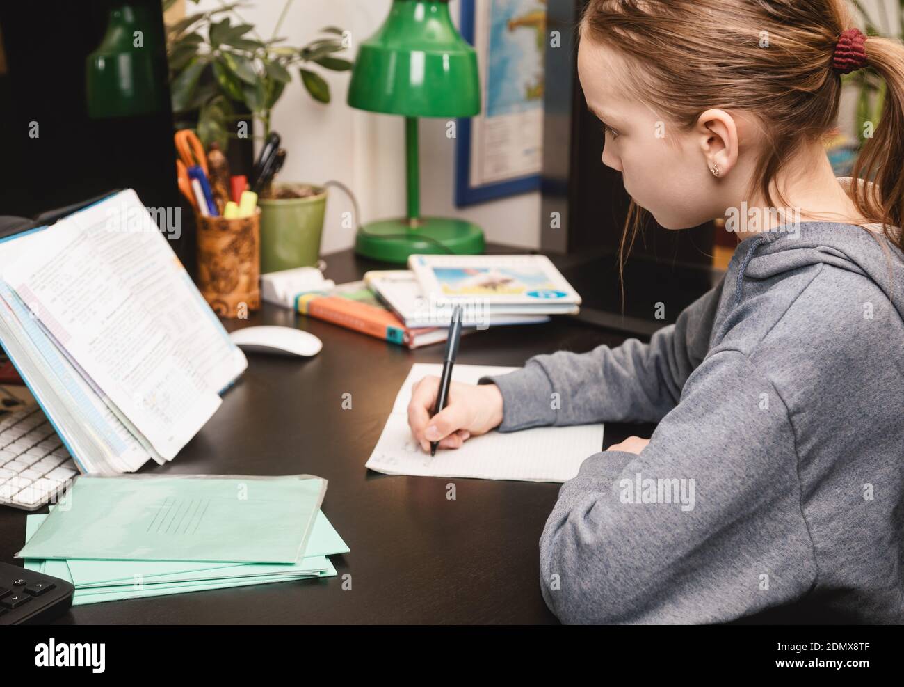 Schulmädchen schreiben in einem Notizbuch sitzen bei einem Schreibtisch studieren Zu Hause Hausaufgaben während Coronavirus COVID-19 Quarantäne Stockfoto