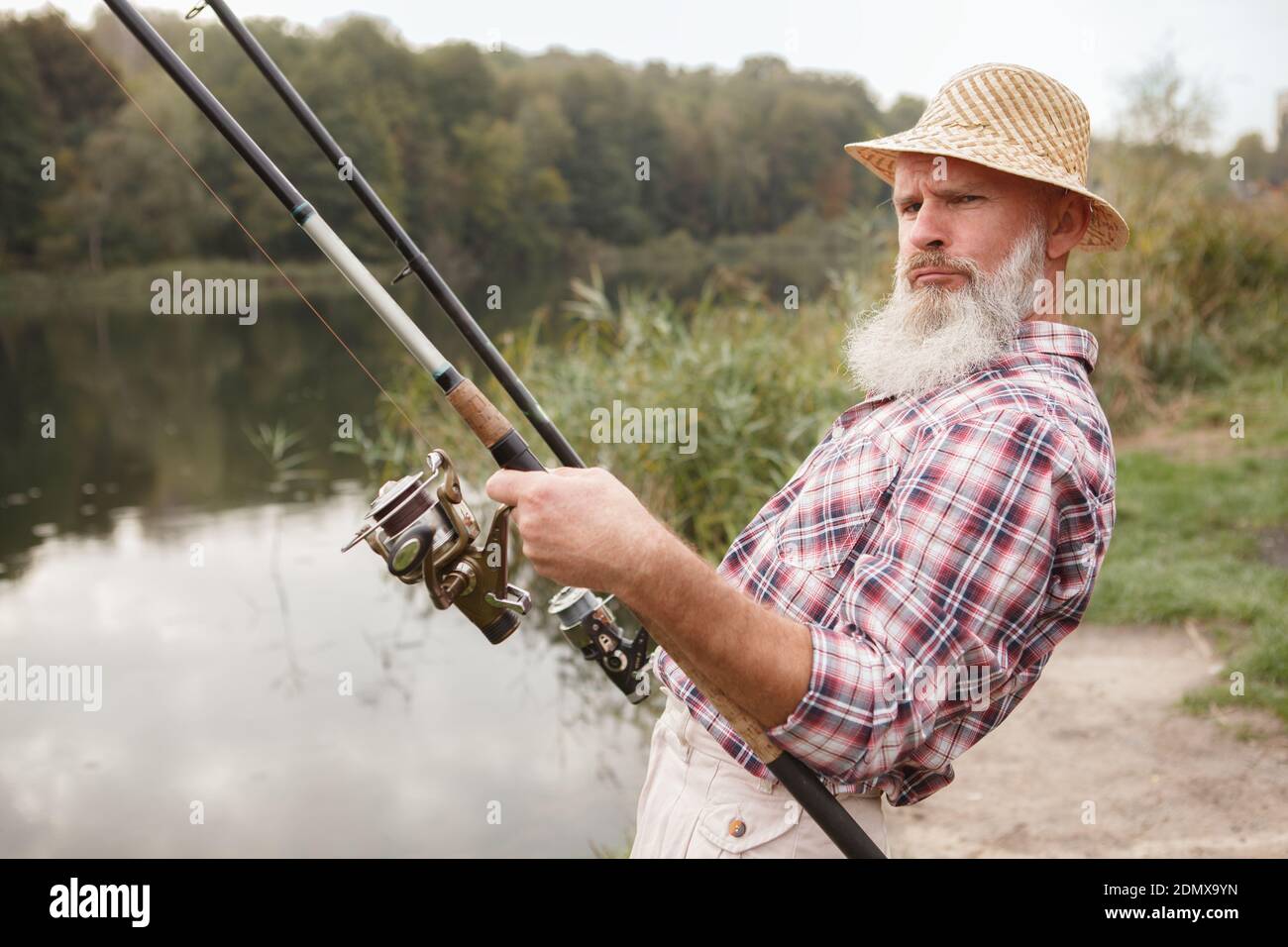 Lustige Opa Angeln mit zwei Spinnruten, so dass kühle Gesicht, entspannen am Fluss Stockfoto