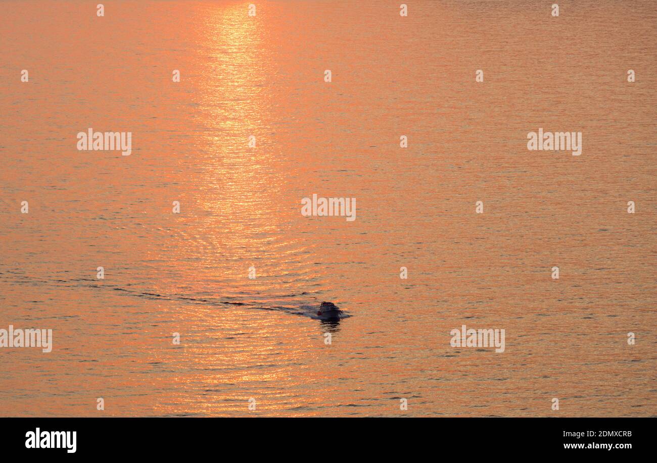 Sveti Stefan, Budva, Montenegro. Kleines Boot, das die ruhigen Gewässer der Budva Bucht überquert, Sonnenuntergang. Stockfoto