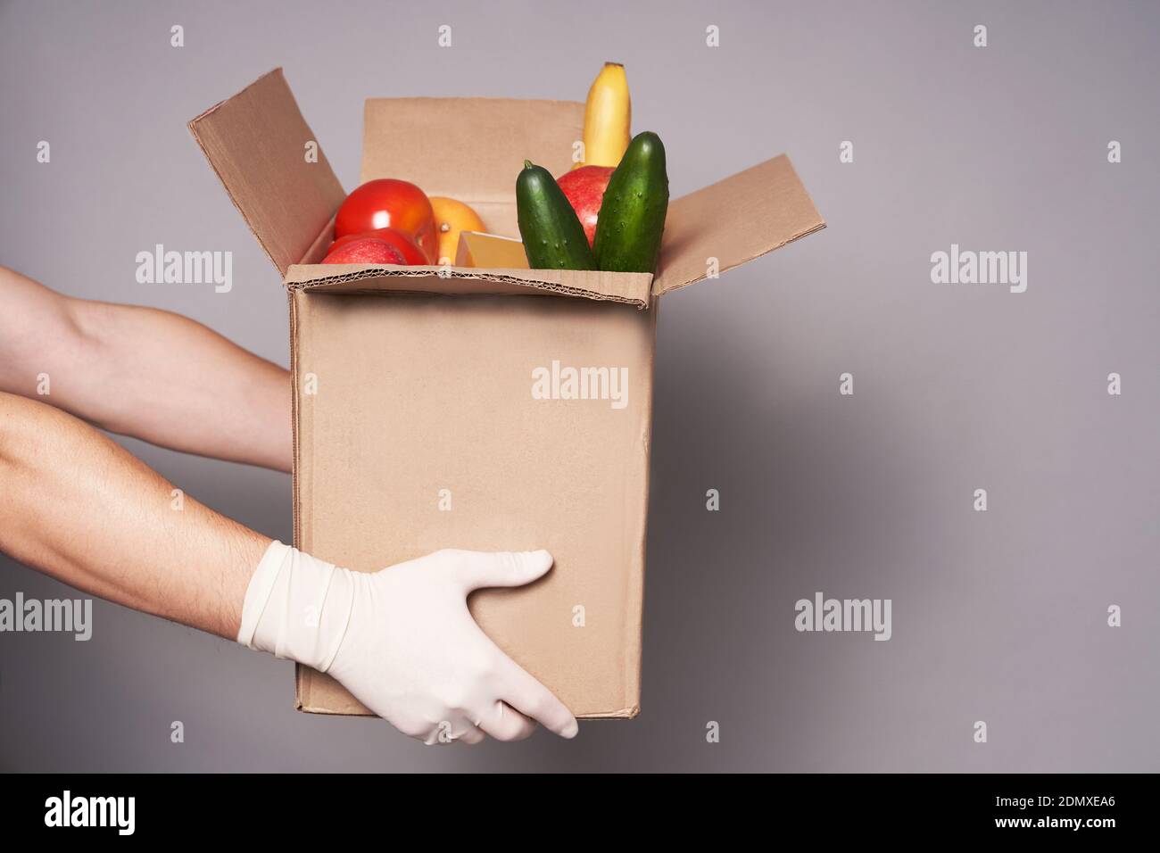 Hände von weißen Kurier in Gummihandschuhen halten einen Karton mit Lebensmitteln, schnelle und sichere Lieferung von Lebensmitteln. Stockfoto