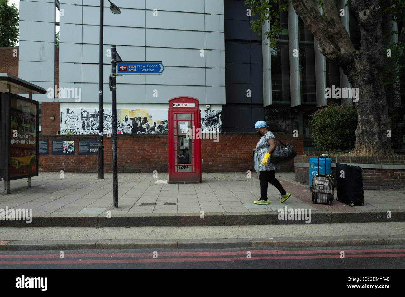 Eine Frau trägt Gummihandschuhe und eine Maske, während sie Wartet auf einen Bus in New Cross Stockfoto