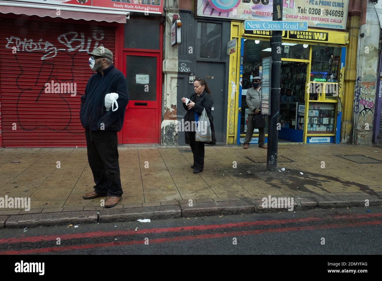 Ein Mitglied der Öffentlichkeit trägt eine Maske, wie er Wartet auf einen Bus auf der New Cross Road während des Coronavirus-Pandemie Stockfoto