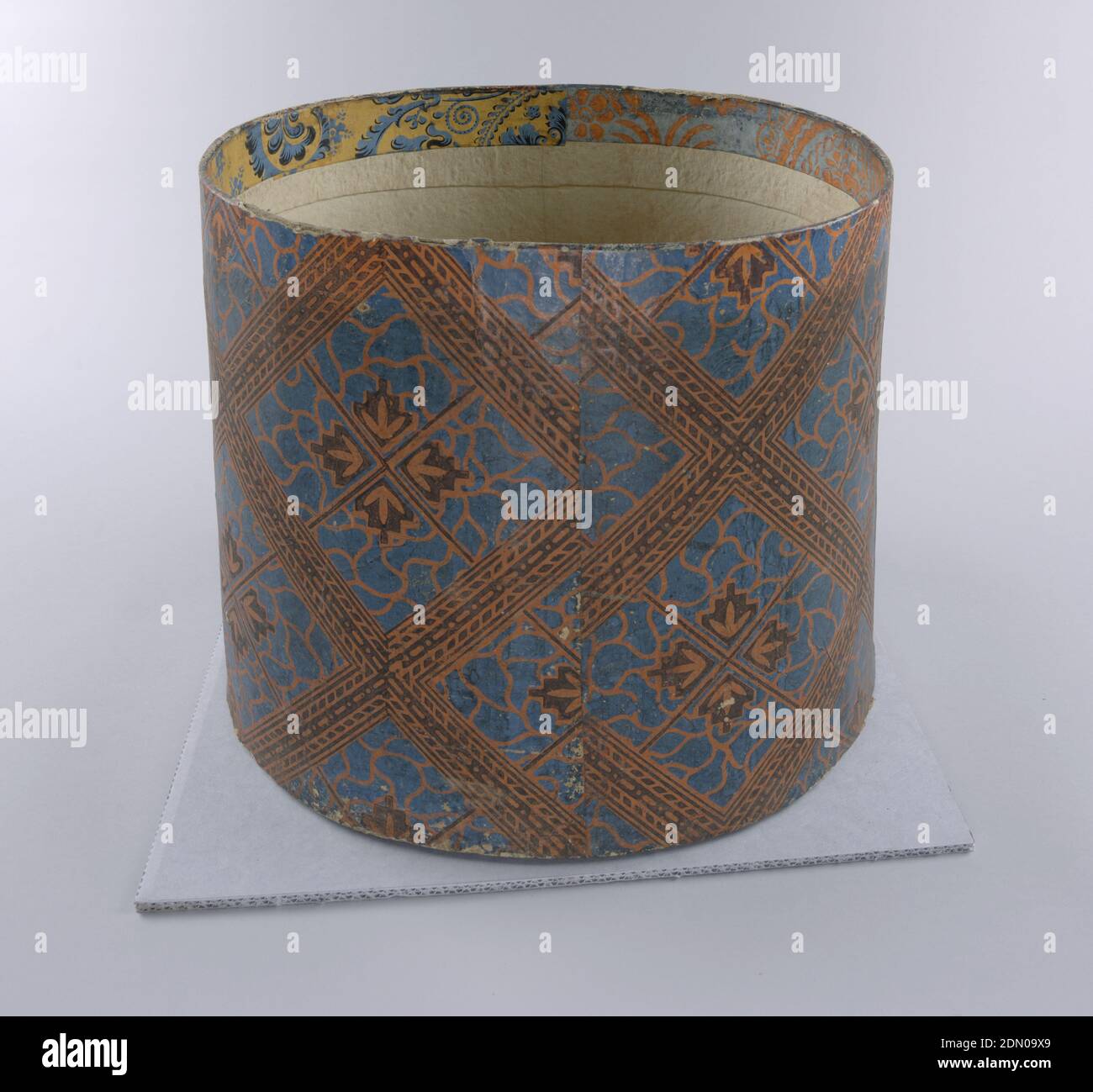 Bandbox, Block-bedrucktes Papier, Pasteboard Unterstützung, hohe Karton Bandbox mit Tapete von geometrischen Lachs und blauen Muster bedeckt, mit braun. Quadratische, große Diamantformen mit algenartigen Füllungen und symmetrischen Blüten- oder Blattformen. Innen Rand, Fragmente von zwei verschiedenen Tapeten Muster, ein Lachs auf hellblau, ein blau auf gelb. Zwei hölzerne Verstrebungen quer., USA, 1835–38, Wandbeläge, Bandbox Stockfoto