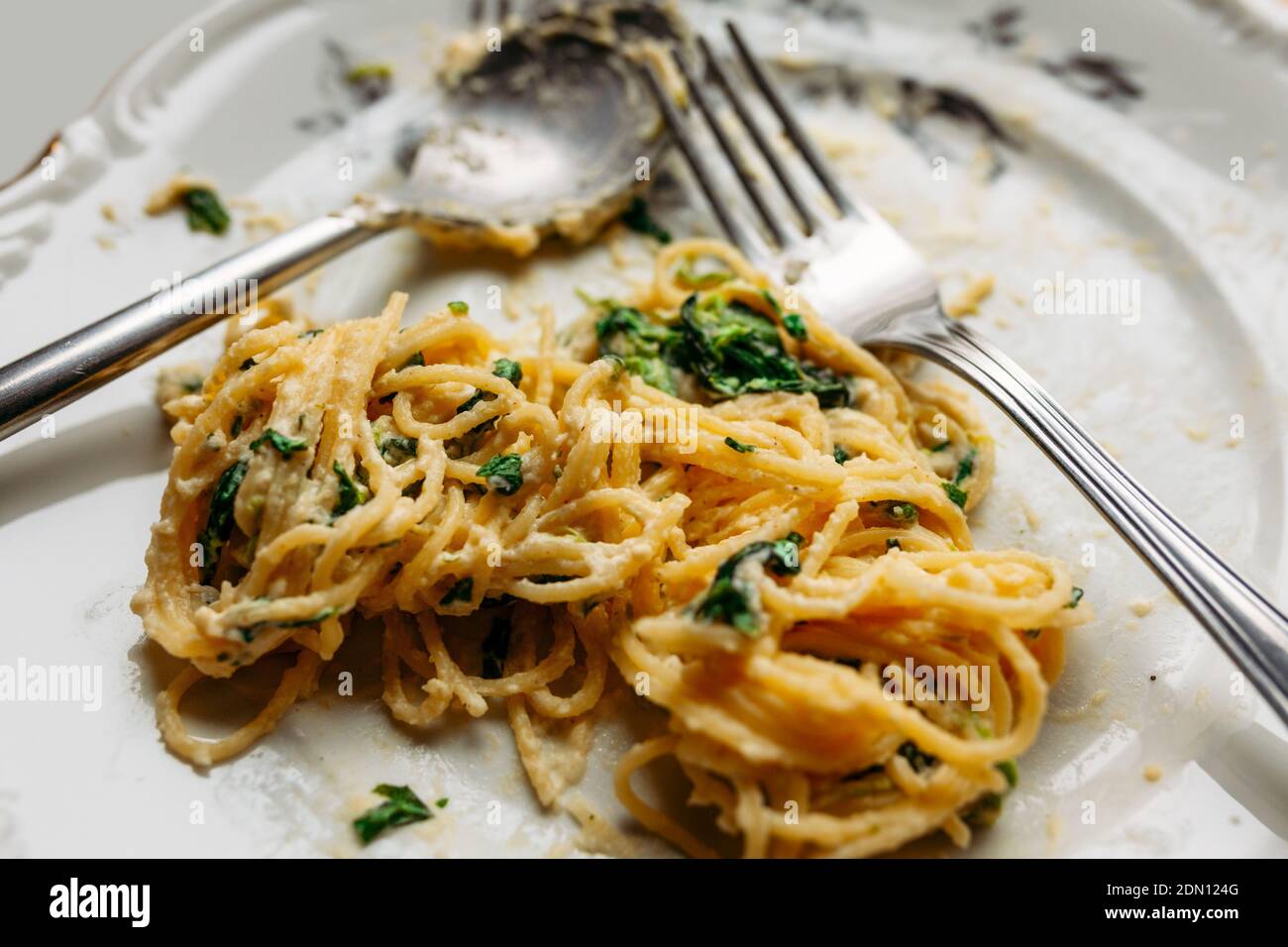 Spaghetti in cremiger Spinat-Sauce mit Käse, auf einem unordentlichen Blumenplatte mit silberner Gabel und Löffel, halb gegessen, Nahaufnahme Stockfoto
