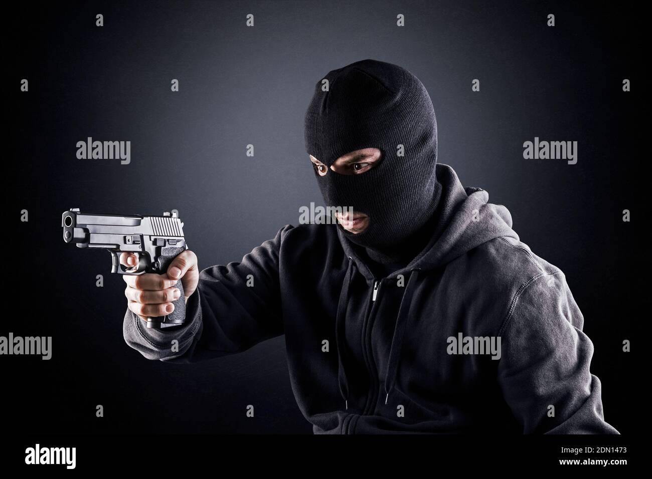 Criminal trägt schwarze Balaclava und Kapuzenpullover mit einer Waffe in Die Dunkelheit Stockfoto