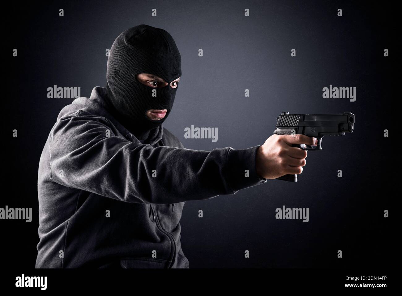 Criminal trägt schwarze Balaclava und Kapuzenpullover mit einer Waffe in Die Dunkelheit Stockfoto