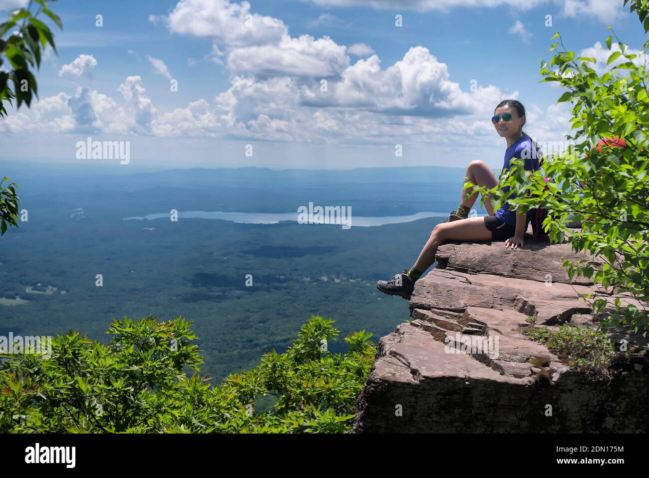 Eine chinesin, die an einem sonnigen Sommertag am Rande einer Klippe auf einem Aussichtspunkt in den catskills in Woodstock New York sitzt. Stockfoto