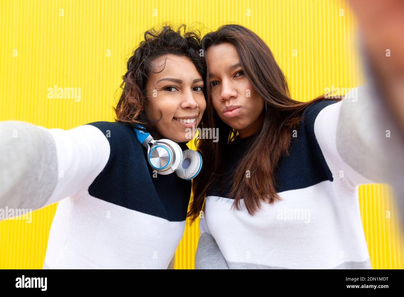 Zwei lustige hispanische Mädchen machen Selfie Foto auf Handy. Sie sind auf einem gelben Hintergrund isoliert. Konzept der Freundschaft. Stockfoto