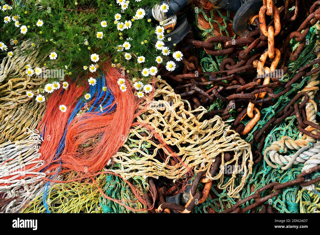 Bunte, entsorgte Fischernetze, verrostete Ketten und Blumen am Meer Stockfoto