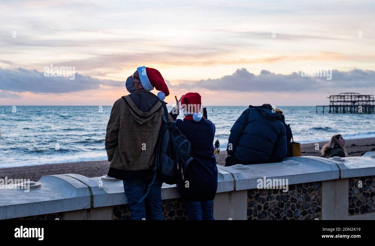 Brighton UK 17. Dezember 2020 - EIN Paar in Santa Hüte machen das Beste aus dem Sonnenuntergang an der Küste von Brighton am Ende eines hellen Tages an der Südküste . Die Stadt Brighton und Hove wurde in Coronavirus Tier zwei Beschränkungen in England nach einer Ankündigung heute von der Gesundheitsminister Matt Hancock gehalten : Credit Simon Dack / Alamy Live News Stockfoto