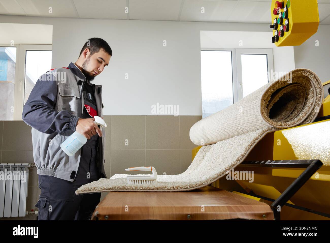 Mann trägt einheitliche Spraying Reinigungsmittel auf blauen Teppich zu entfernen Flecken in professionellen Reinigungsservice Stockfoto