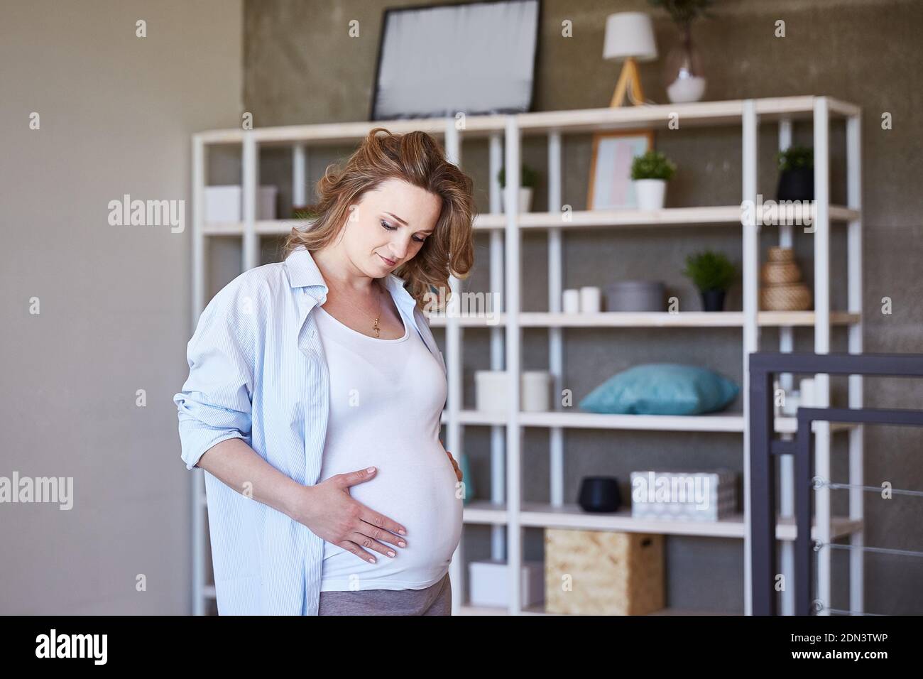 Ein charmantes schwangeres Mädchen schaut auf ihren Bauch und bewundert das Baby in ihrem Bauch. Attraktive Mädchen fühlt sich Glück und gute Gesundheit. Eine schöne Frau Stockfoto