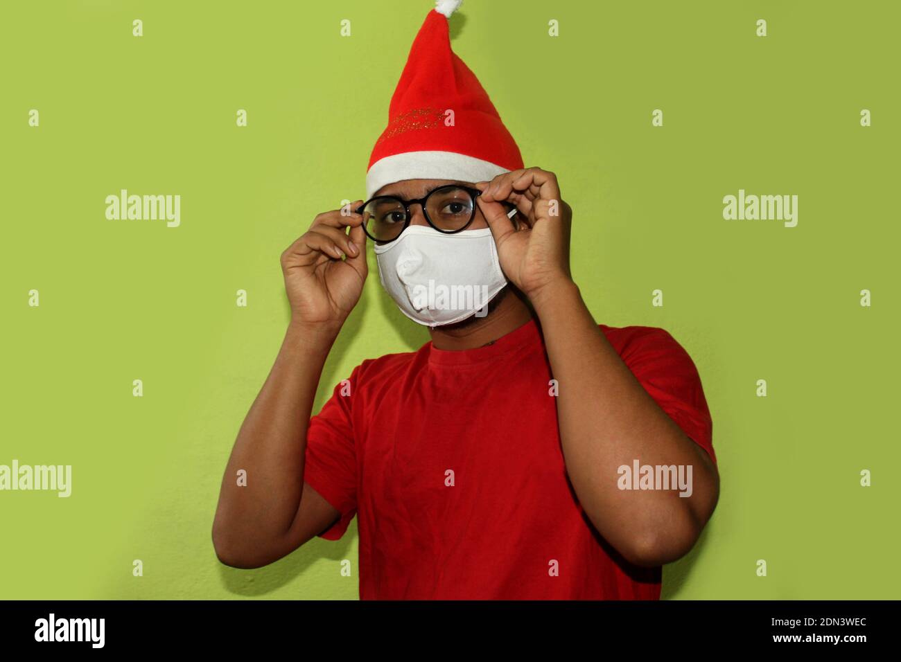 Weihnachten während der Pandemie des COVID-19 Coronavirus. Mann trägt chirurgische Gesichtsmaske und Santa Hut. Männliches Modell mit Brille im weihnachtsmann Kostüm. Stockfoto