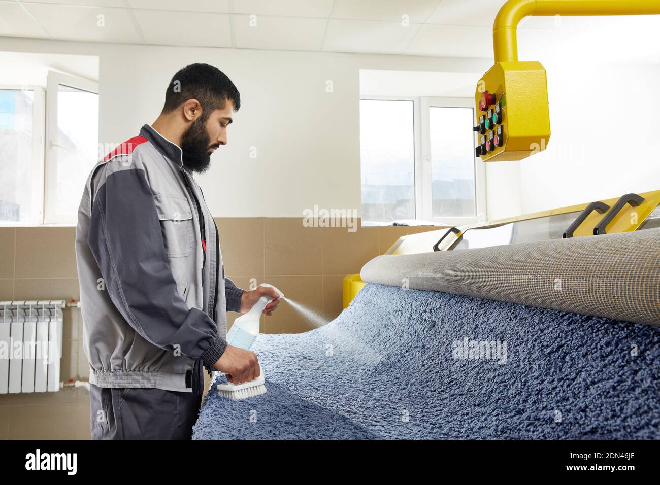 Mann trägt einheitliche Spraying Reinigungsmittel auf blauen Teppich zu entfernen Flecken in professionellen Reinigungsservice Stockfoto