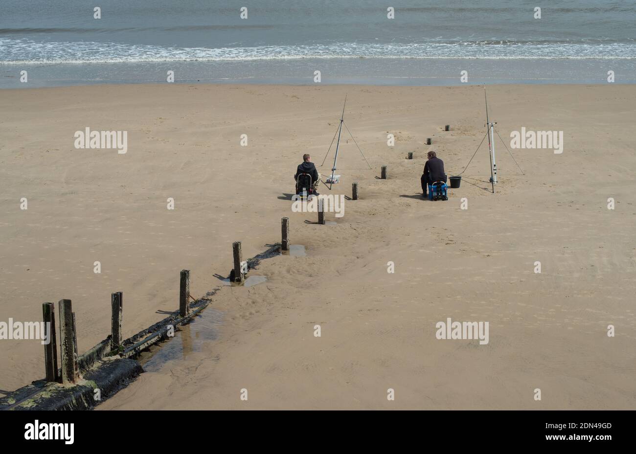 Zwei Angler Angeln vom Strand sitzen auf beiden Seiten Eine alte Stumper und in der Tat sozial distanziert Stockfoto