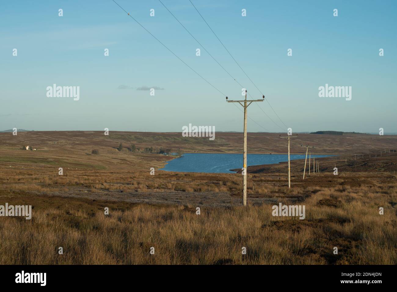 Das Bild zeigt Telegraphenmasten und Telefonleitungen, die sich über offene Strecken erstrecken Moorland mit einem kleinen Stausee in der Ferne Stockfoto
