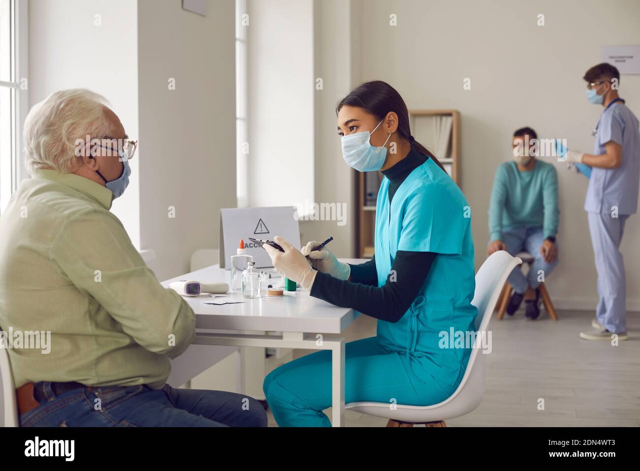 Asiatische Ärztin interviewt einen älteren Mann, der zur Impfung ins Krankenhaus kam. Stockfoto
