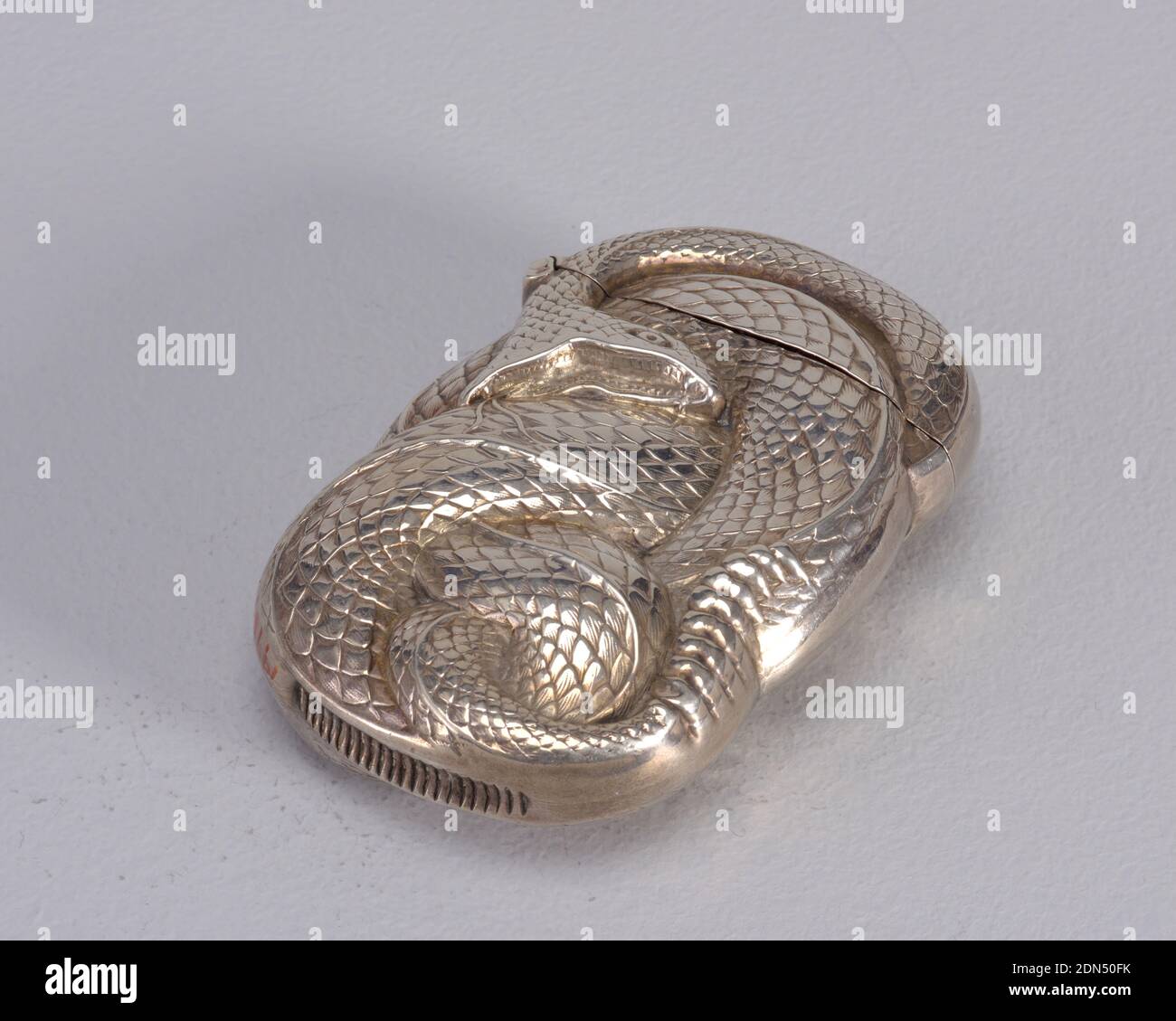 Gewickelte Klapperschlange, William B. Kerr & Company, amerikanisch, 1855 - 1927, Silber, Oblong, mit unregelmäßigen gekrümmten Seiten, die sich der Form der gewickelten Klapperschlange anpassen, der Mund ist offen, die Fangzähne sind dargestellt, die Gabelzunge ist ausgefahren, die Rassel am Ende des Schwanzes, die gesamte erhabene Schuppenstruktur, um Schlangenhaut zu simulieren, identische Dekoration auf der Rückseite. Deckel seitlich aufklappbar. Schließbügel in versenkter Nut unten, ca. 1890, Container, Dekorative Kunst, Matchsafe, Matchsafe Stockfoto