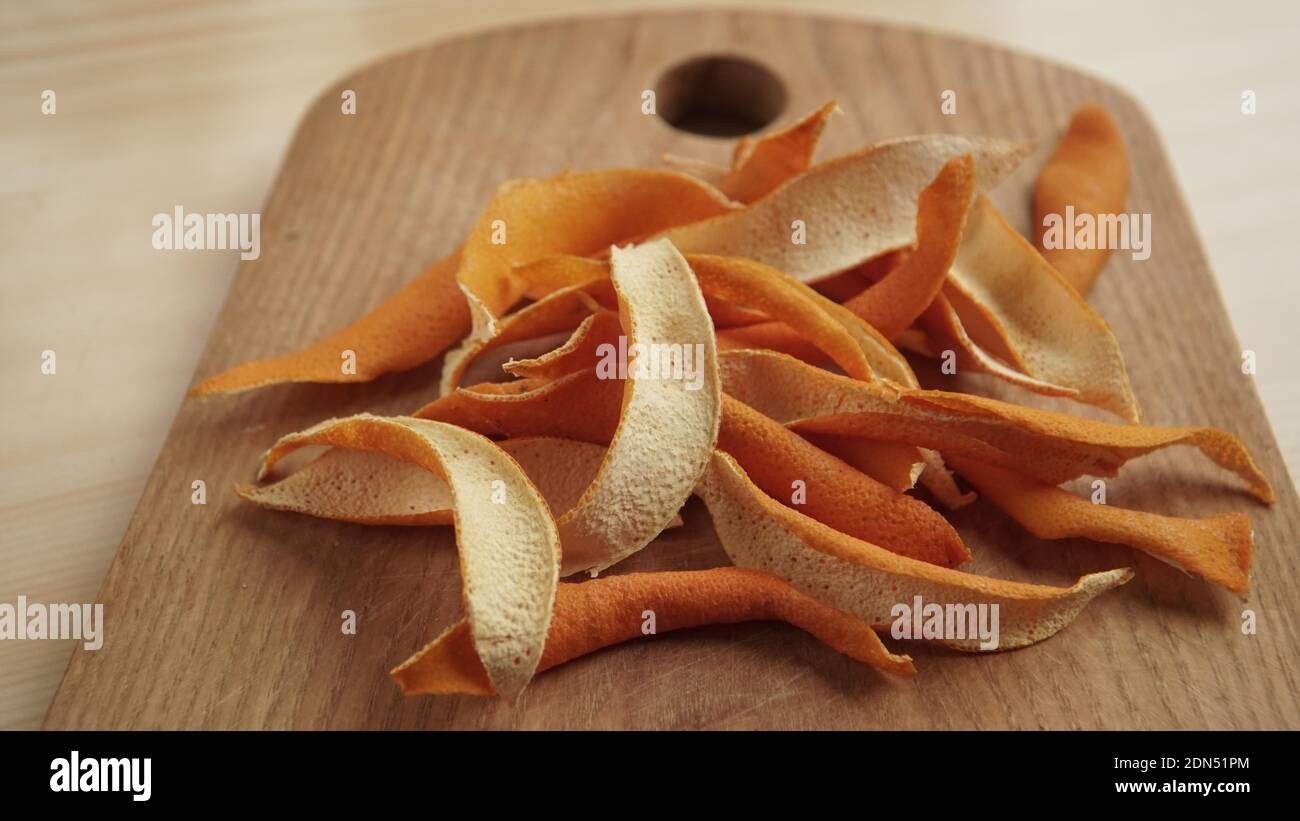 Die getrocknete Orange schält sich auf einem hölzernen Kochbrett in einer Nahaufnahme. Eine Möglichkeit, Geschmack zu der Mahlzeit hinzuzufügen. Trockene Frucht Gewürze Struktur. Essen natürliche Aromen Stockfoto