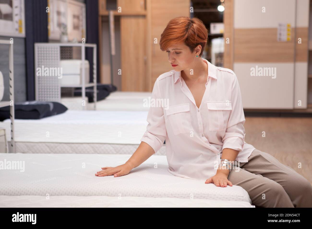 Attraktive weibliche Kundin, die neue orthopädische Bett auf Verkauf im Möbelhaus, Kopieplatz Stockfoto