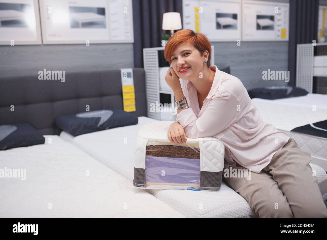 Charmante Frau lächelt die Kamera bei der Wahl neuer orthopädischen Bett zu Hause Waren zu kaufen Stockfoto