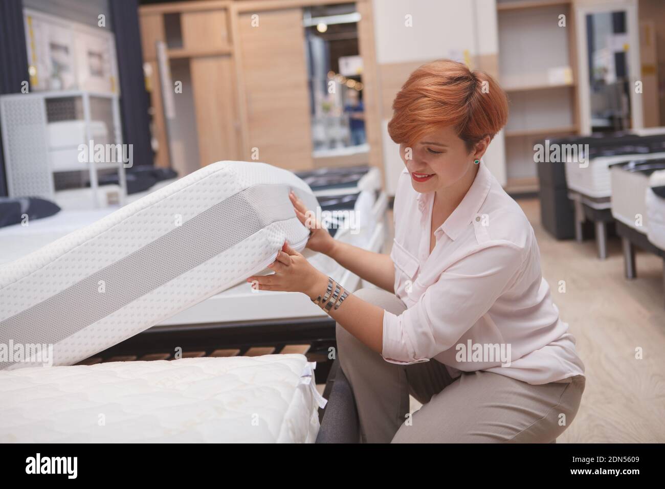 Fröhliche junge Frau lächelnd, die Wahl neue orthopädische Matratze zu kaufen Stockfoto
