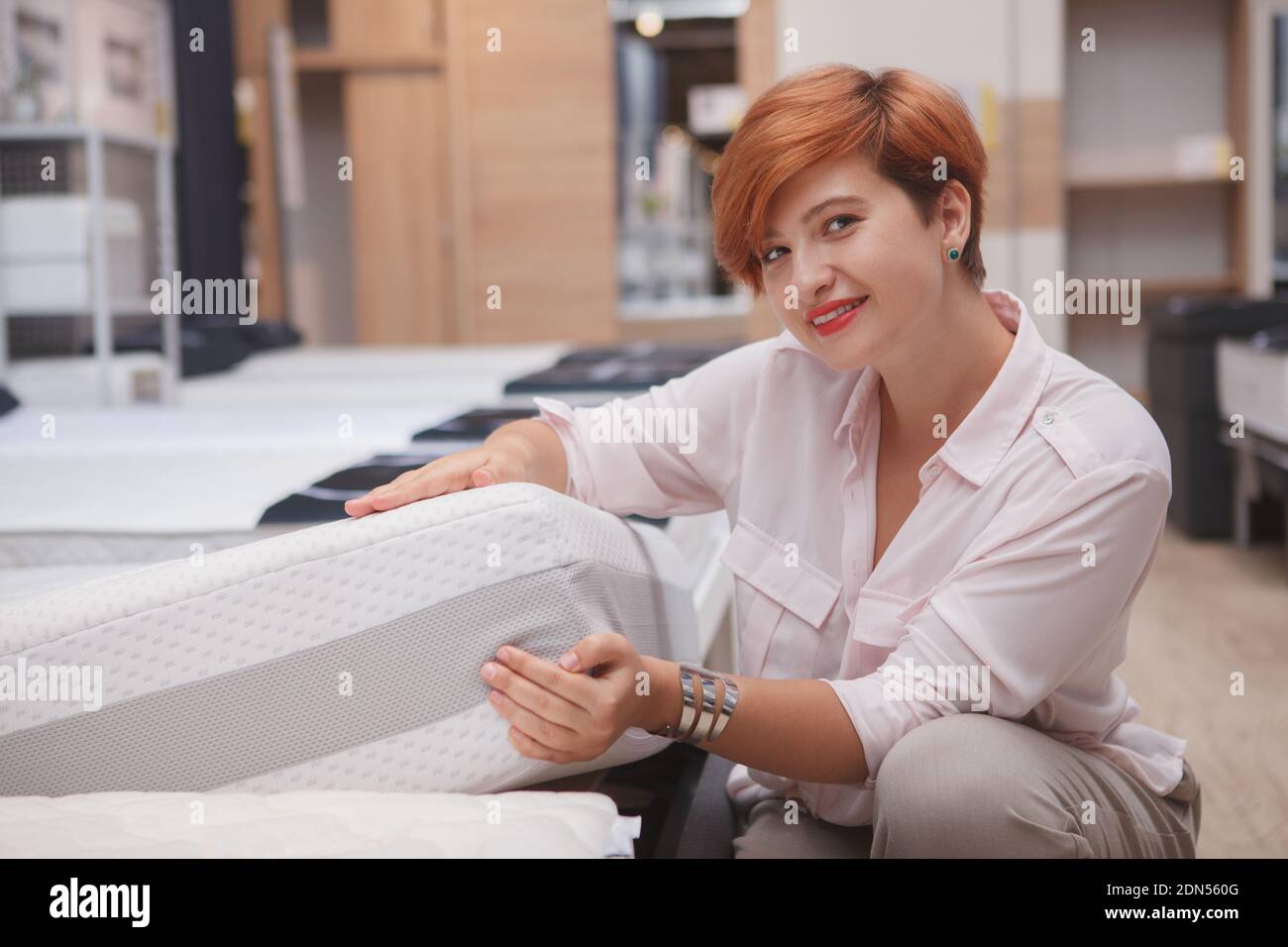 Schöne attraktive junge Frau lächelt an die Kamera, Untersuchung orthopädische Matratze auf Verkauf, Kopierer Raum Stockfoto