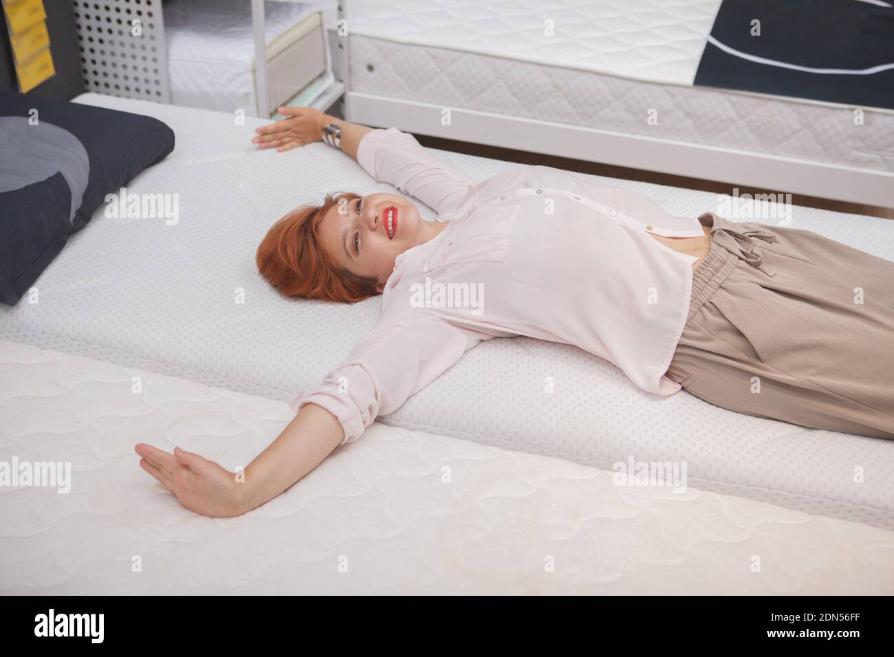 Aufgeregt junge Frau streckt ihren Rücken liegend auf orthopädische Matratze Im Möbelgeschäft Stockfoto