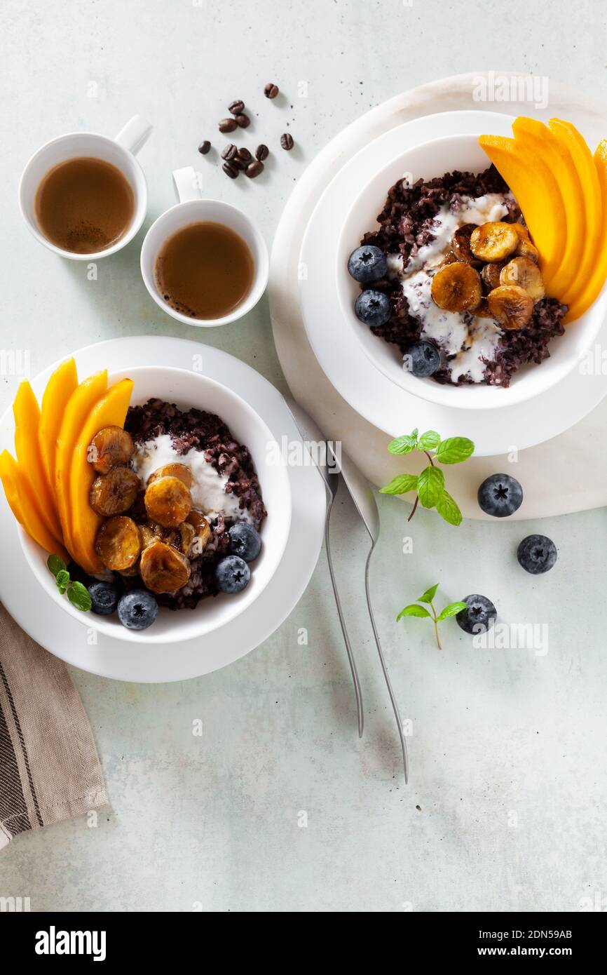 Karibisch süßes Frühstück aus schwarzem Reisbrei mit Kokosmilch und Mango, gebratene Bananen. Gesunde jamaikanische Küche. Und Kaffee Stockfoto