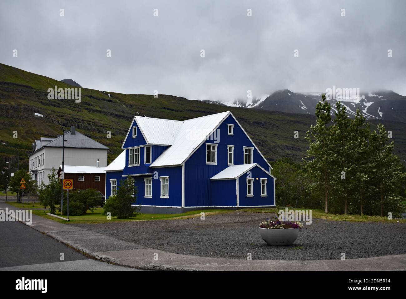 Ein helles blau-weißes Gebäude in der kleinen Stadt Seydisfjordur in der Region Eastfjords in Island. Schneebedeckte Berge verschwinden in den Wolken. Stockfoto