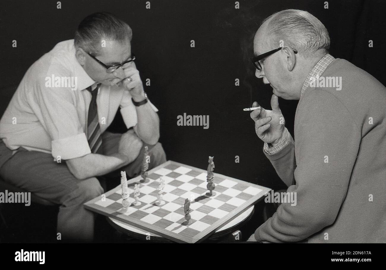 1960er, historisch, zwei ältere Männer, die sich konzentrieren, während sie sich gegenübersitzen und ein Schachspiel spielen, wobei das Schachbrett auf einem kleinen Couchtisch zwischen ihnen saß und nur noch ein paar Stücke auf dem Spielbrett lagen, England, Großbritannien. Ein beliebtes Brettspiel, ein abstraktes Strategiespiel, die moderne Version aus dem 15.. Jahrhundert, Schach wird auf einem 64 Quadratmeter großen Schachbrett mit 16 Steinen gespielt, der Gewinner greift den König des Gegners an und schachmatt ihn, sodass es keine Möglichkeit gibt, auf dem Brett zu entkommen. Stockfoto