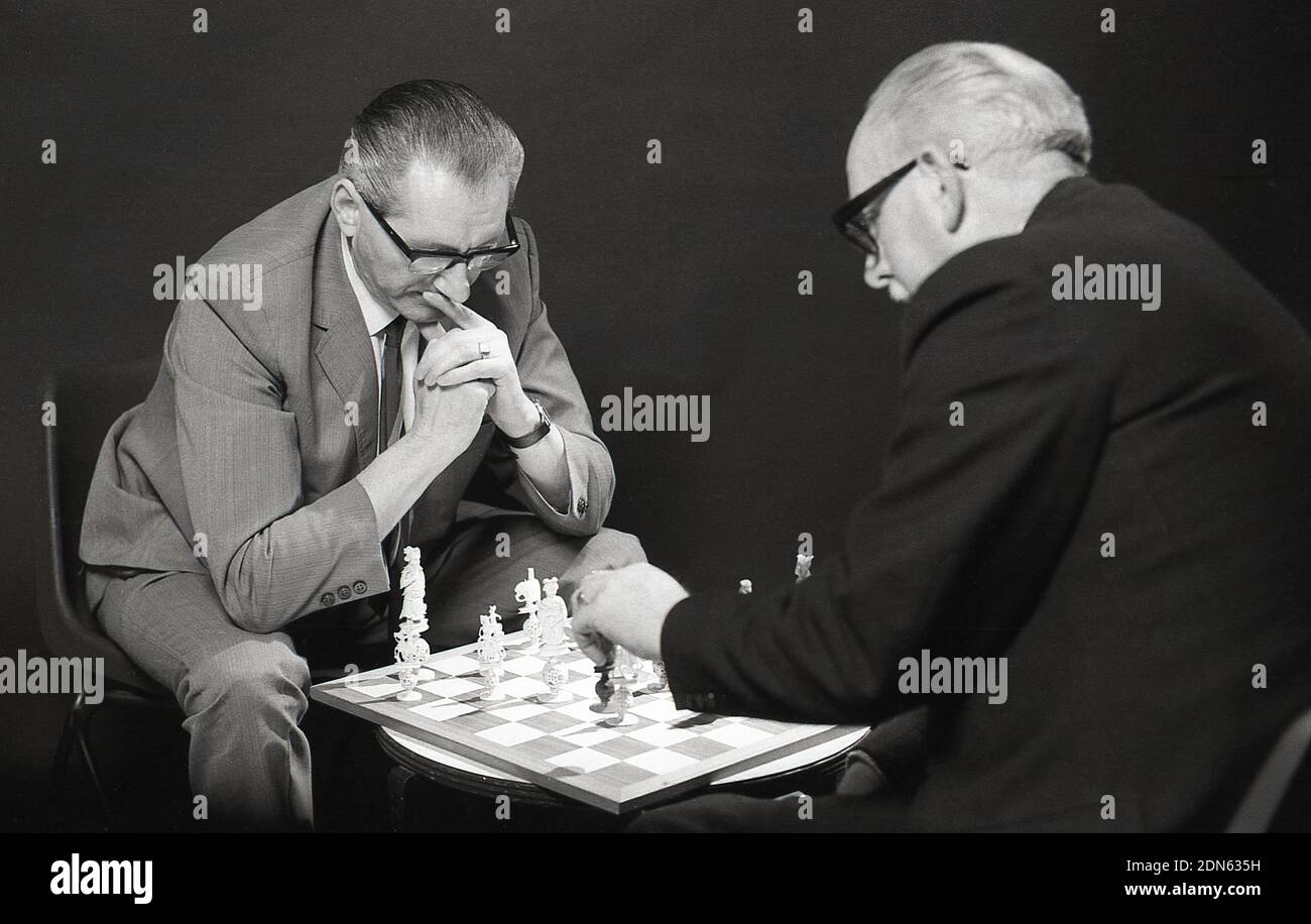 1960er, historisch, zwei ältere Männer, die sich konzentrieren, sich gegenübersitzen und ein Schachspiel spielen, mit dem Schachbrett auf einem kleinen Kaffeetisch, zwischen ihnen, England, Großbritannien. Ein beliebtes Brettspiel, ein abstraktes Strategiespiel, die moderne Version aus dem 15.. Jahrhundert, Schach wird auf einem 64 Quadratmeter großen Schachbrett mit 16 Steinen gespielt, der Gewinner greift den König des Gegners an und schachmatt ihn, sodass es keine Möglichkeit gibt, auf dem Brett zu entkommen. Da das Spiel eine Kombination aus Logik, Mustern, Fokus, Gedächtnis und Entscheidungsfindung beinhaltet, ist Schach eine gute Übung für das Gehirn. Stockfoto