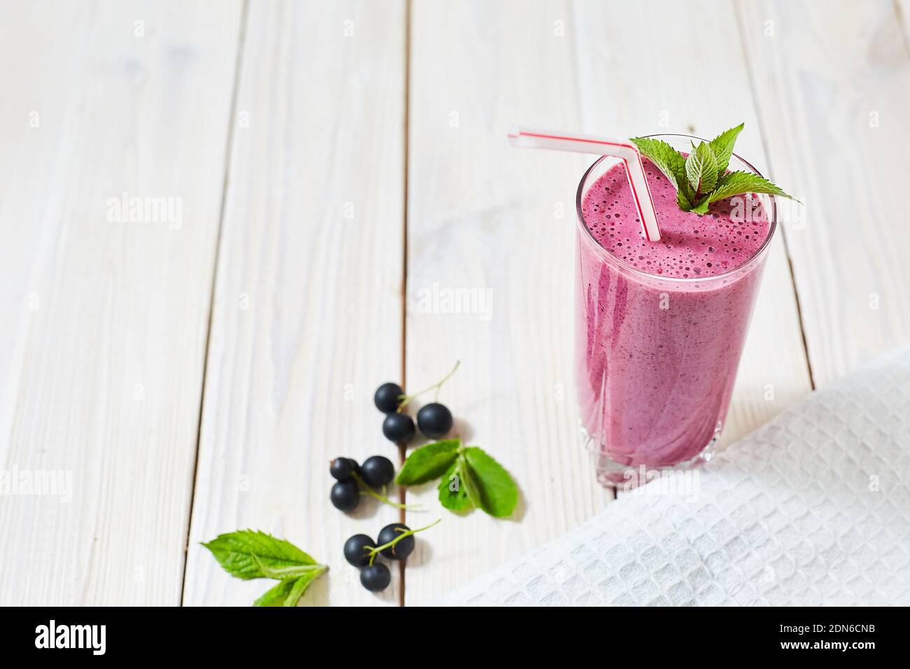 Vitamin Cocktail aus schwarzen Johannisbeeren, Eis, Milch in einer Glastasse. Kunststoffrohr und Minze. Holz weiß Hintergrund und Geschirrtuch. Horizontales Bild Stockfoto
