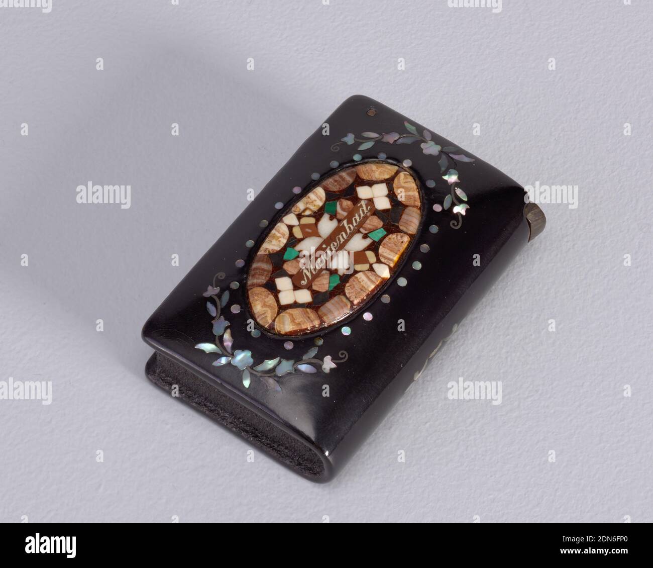 Marienbad', Lack mit Perlmutt-Intarsien und verschiedenen Steinen, rechteckige, abgerundete Ecken, in Buchform, mit zentralem ovalem Reserve mit verschiedenen Intarsiensteinen, horizontal eingeschrieben 'Marienbad'; Reserve mit Perlmutt-Blumenschmuck eingerahmt; Buchrücken oder Unterseite mit Perlmutt-Dekorationsmotiv verziert; Rückseite mit Perlmutt-Blumenzweig. Klappdeckel auf einfachem Metallstift auf der rechten Seite. Stürmer oben und links., Europa, Ende des 19. Jahrhunderts, Container, Dekorative Kunst, Matchsafe Stockfoto