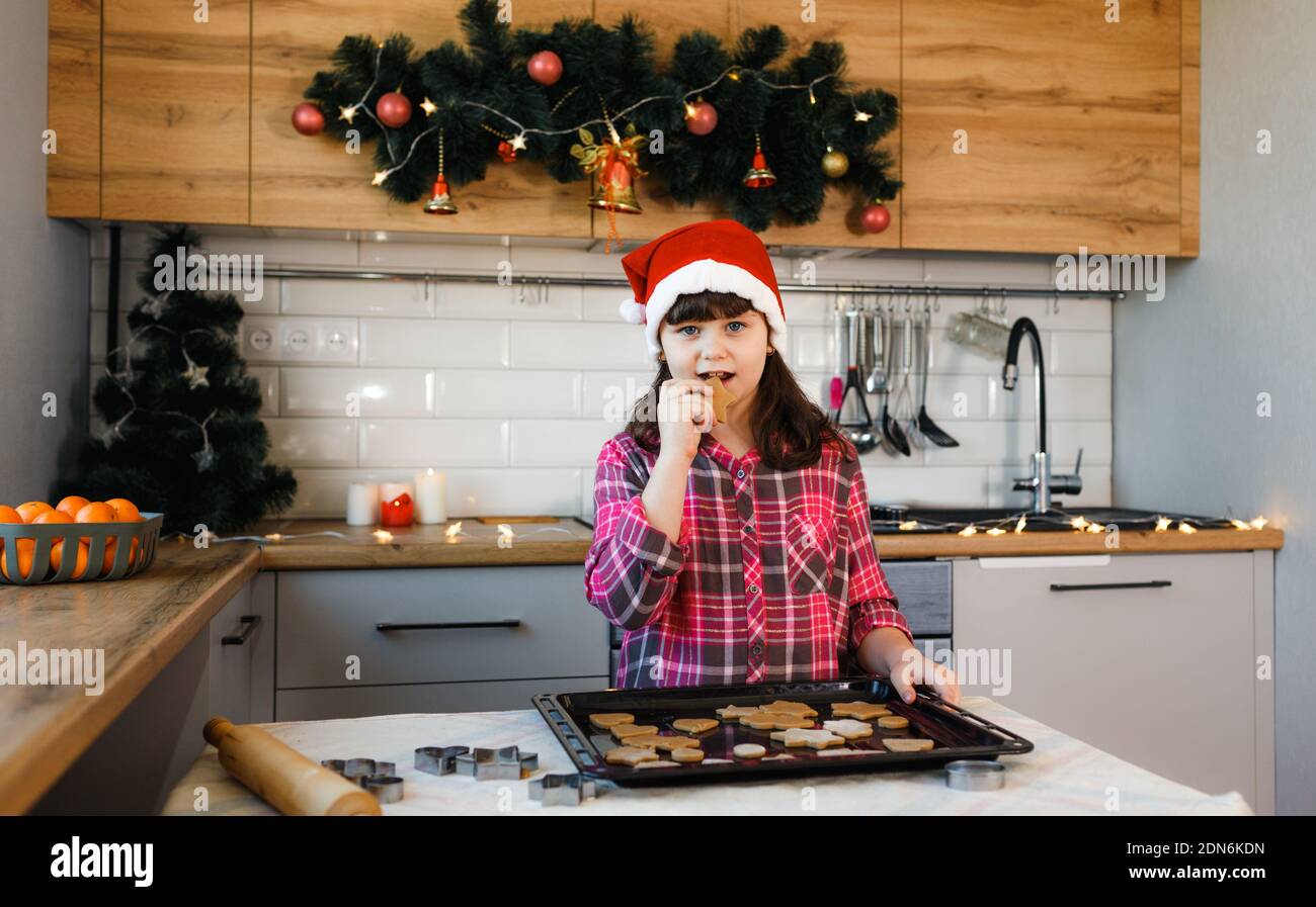 Das Mädchen in der Küche steht neben dem Tablett und Schmeckt die Kekse Stockfoto