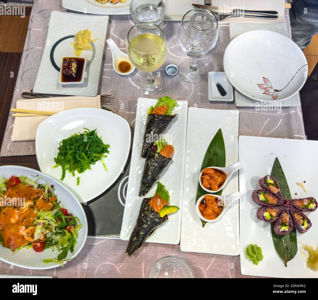 Japanische Wohnung lag auf einem Tisch voller köstlicher Gerichte. Uramaki von Garnelen Tempura, Temaki Reiskegel, frischer Lachs Tartar, Algen mit Sojasauce Stockfoto