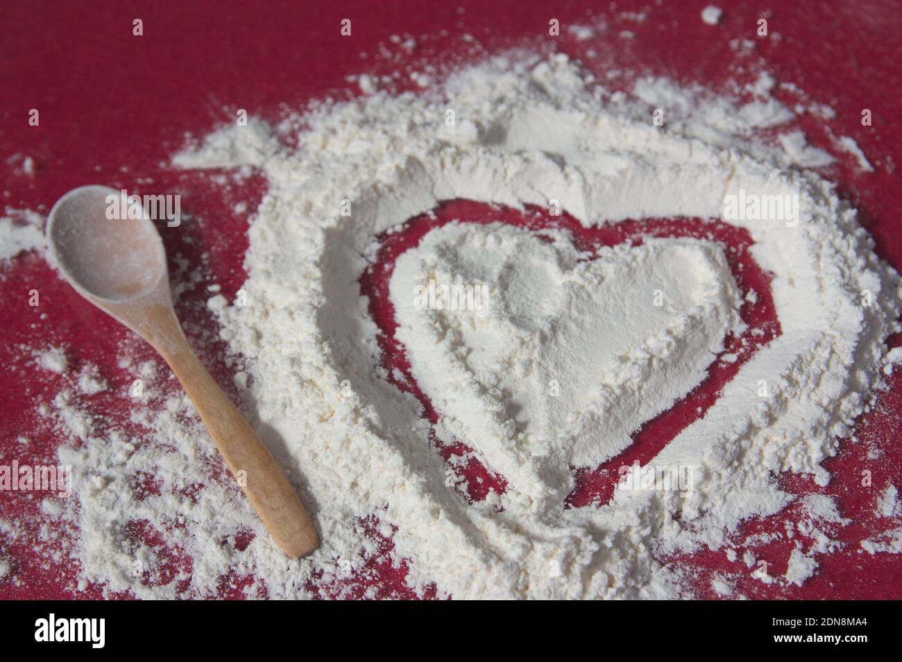Kneading table in which a heart has been drawn on a pile of flour next to a wooden spoon Stockfoto