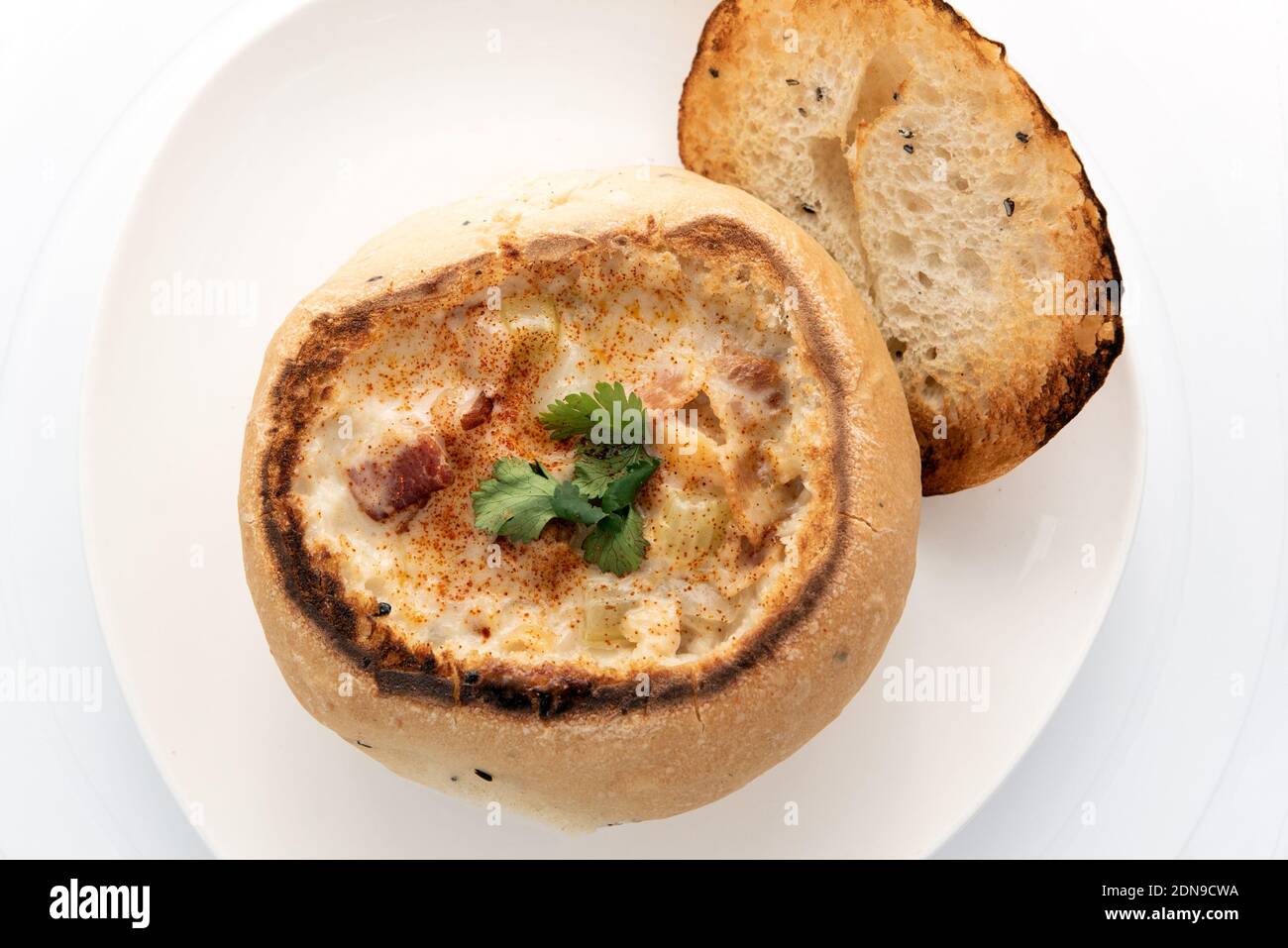 Blick von oben auf eine Schüssel mit herzhafter Muschelsuppe, die in einer im Ofen gebackenen Brotschale enthalten ist. Stockfoto