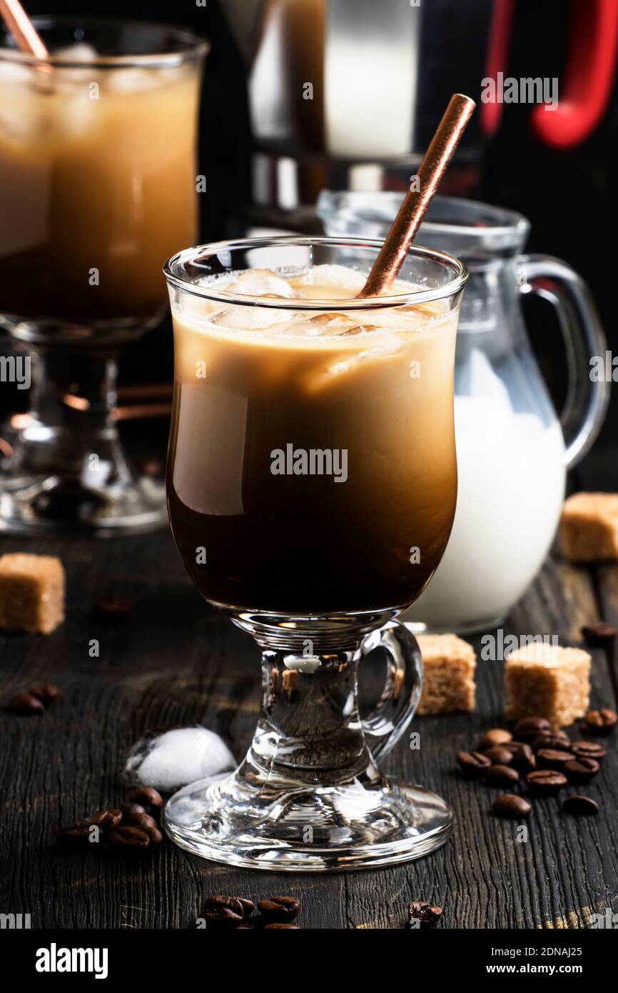 Eiskaffee im Glas, Milch, Zucker und Kaffeemaschine, dunkler Hintergrund, selektiver Fokus Stockfoto