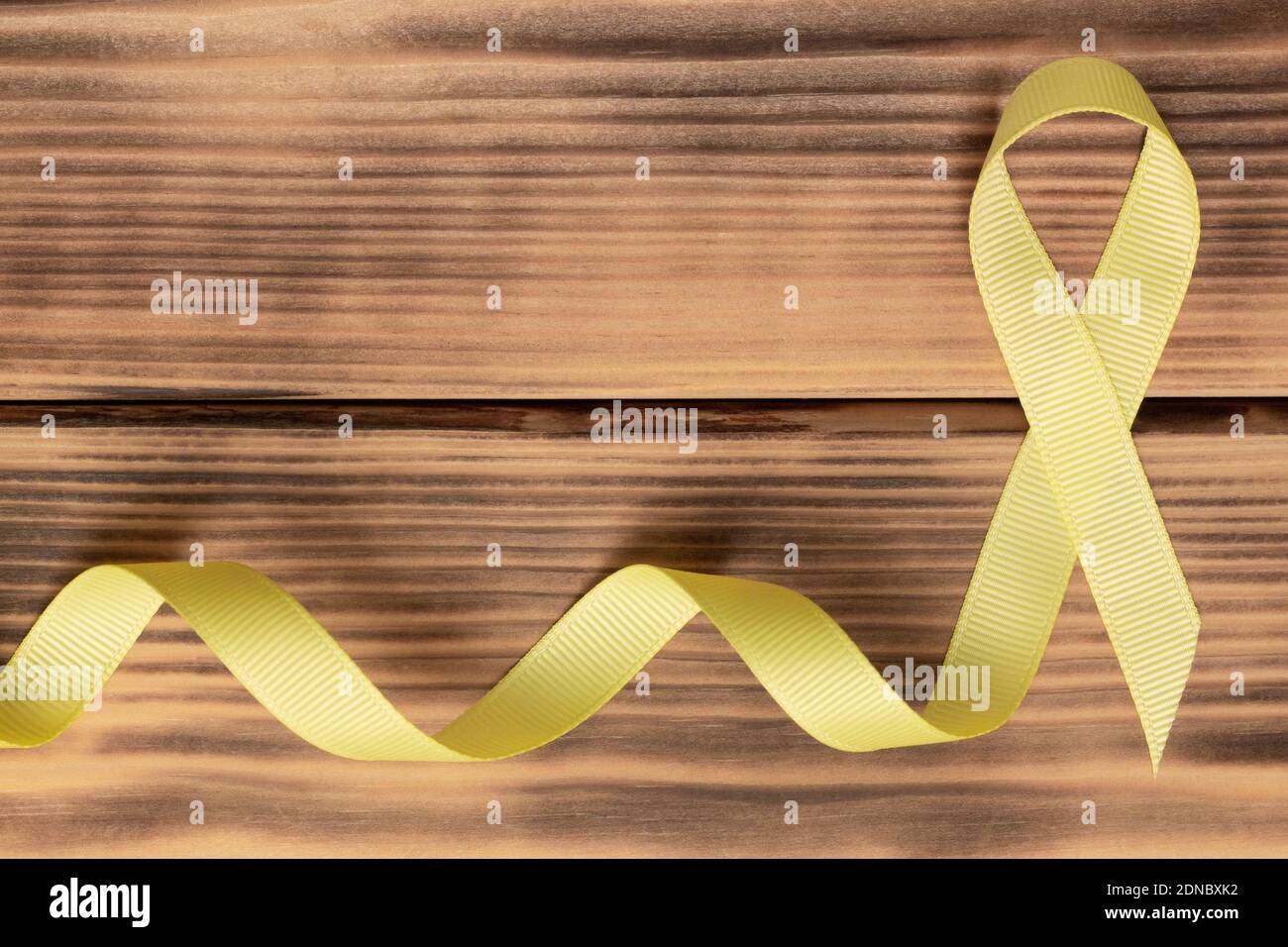 Gelbes Bewusstseinsband, auf Holzhintergrund. Sarkom. Krebs im Kindesalter. Weltkrebstag. Flach liegend. Speicherplatz kopieren Stockfoto