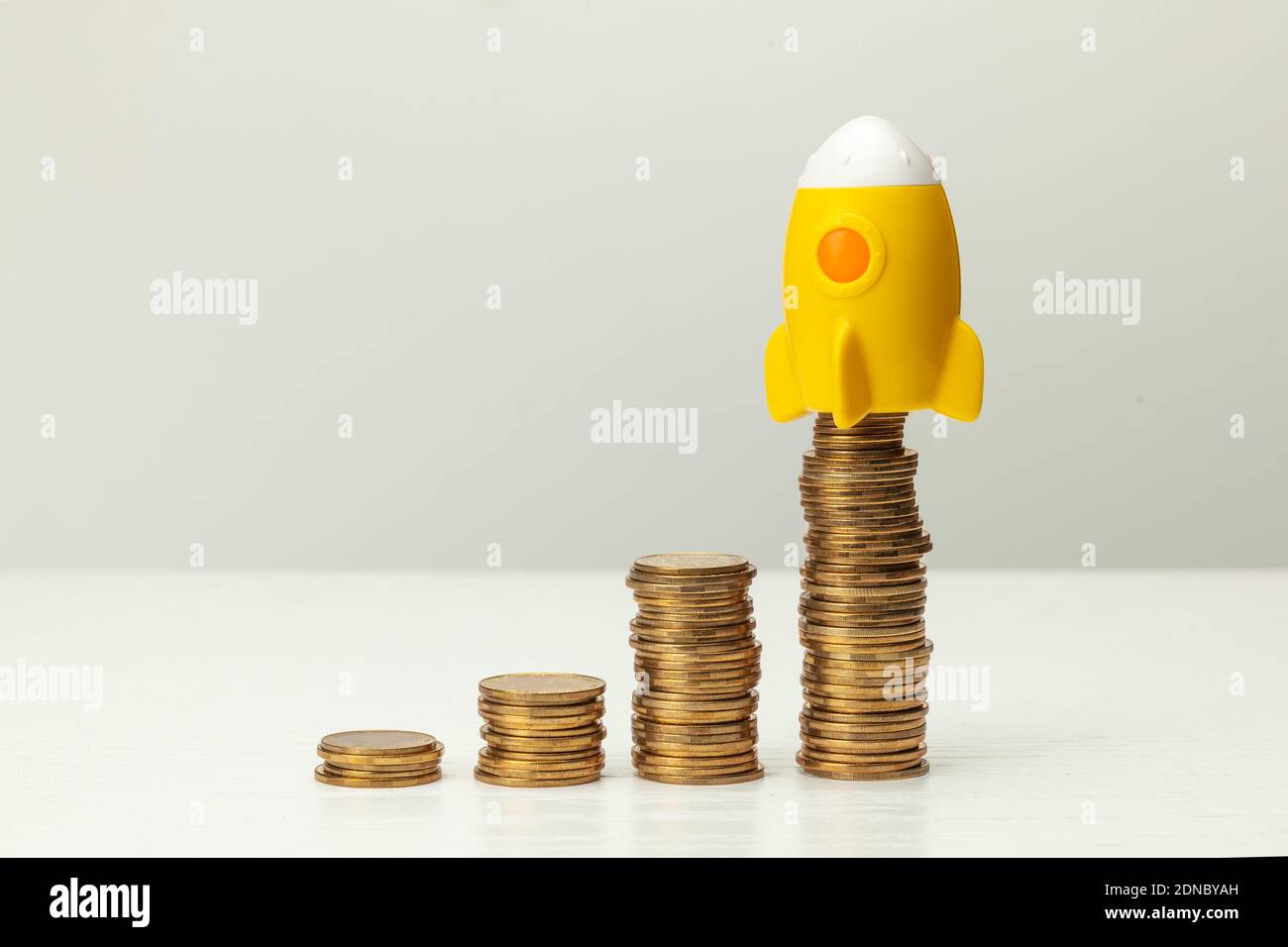 Rakete und Stapel von Goldmünzen auf einem grauen Hintergrund. Konzept für Gewinnwachstum. Stockfoto