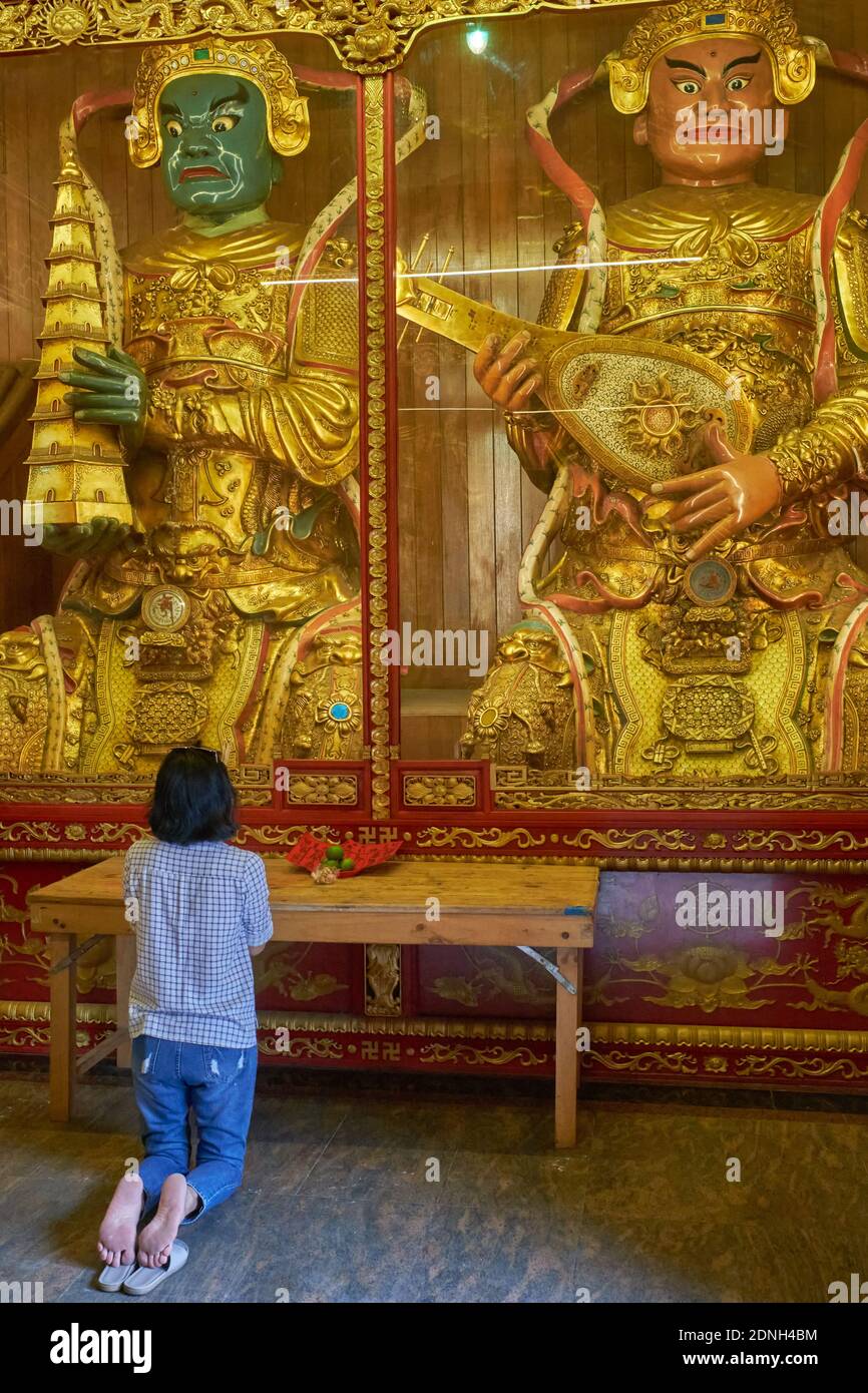 Eine Frau, die vor großen Statuen taoistischer Götter kniet und betet, im Wat Mangkon Kamalawat (Wat Leng Noei Yi) in Chinatown, Bangkok, Thailand Stockfoto