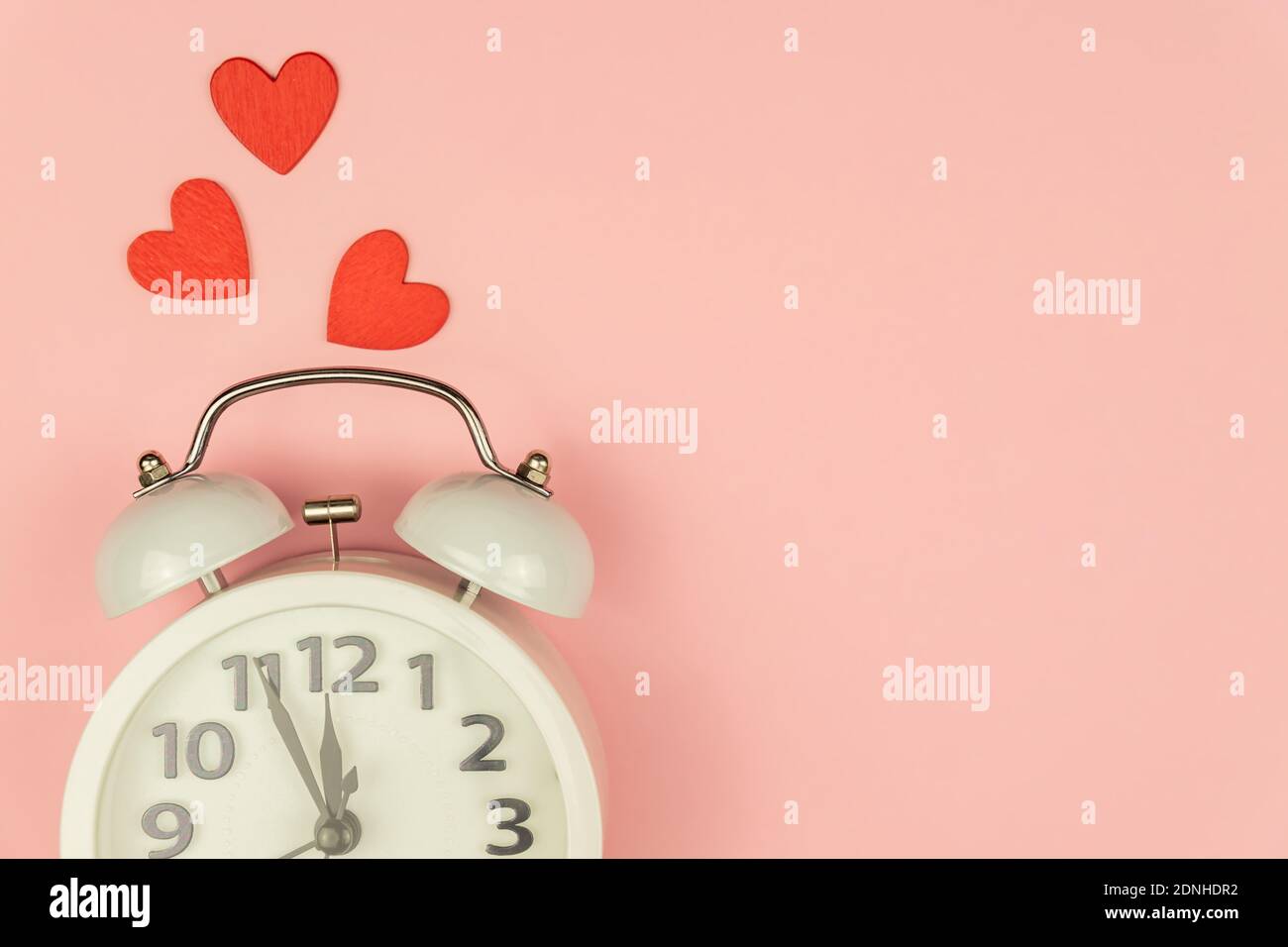 Rosa Hintergrund mit weißem Wecker und roten Herzen. Kreatives Layout. Draufsicht. Zeit für Liebe und Grüße Stockfoto